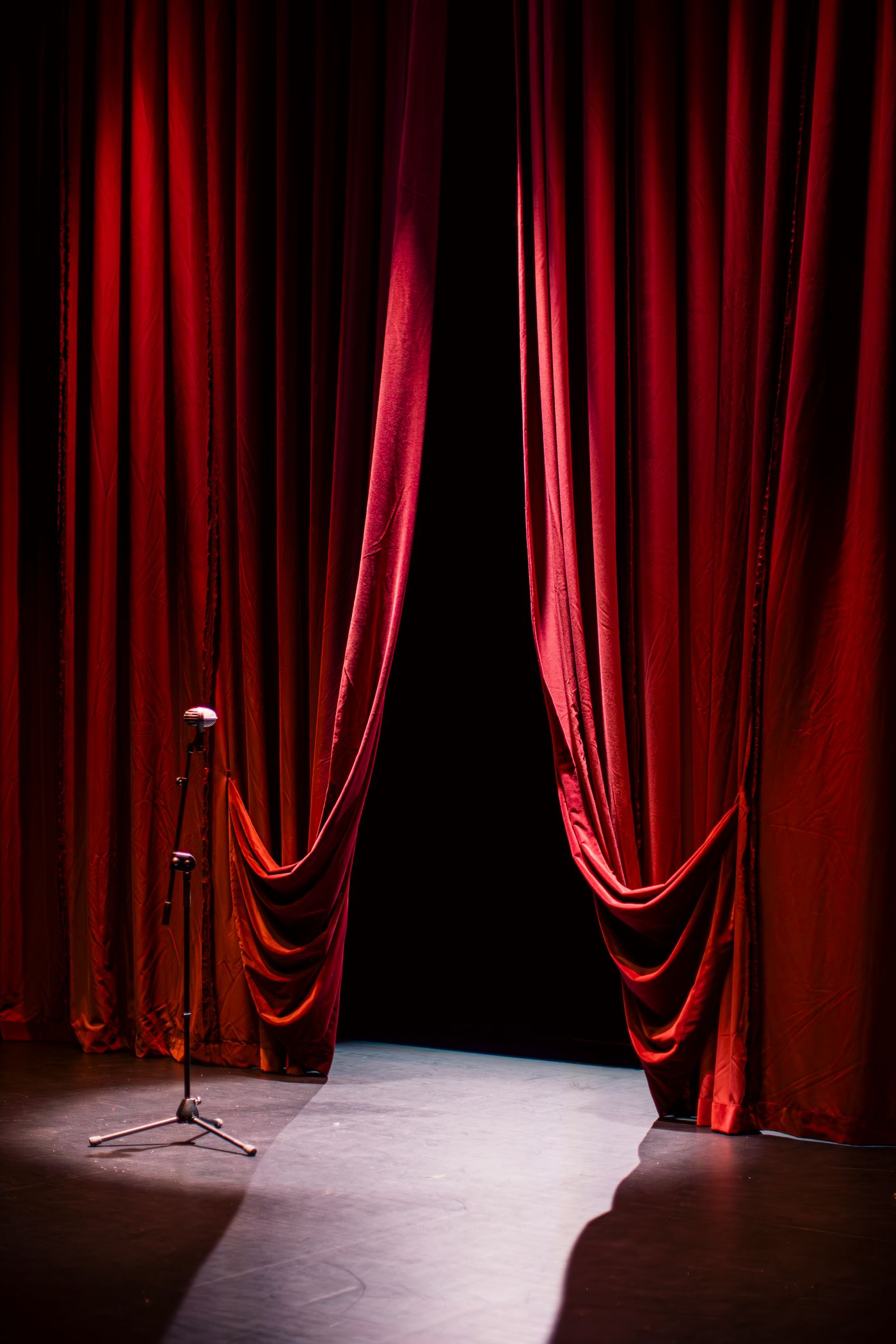 Red velvet theatre curtains opening onto a spotlighted stage